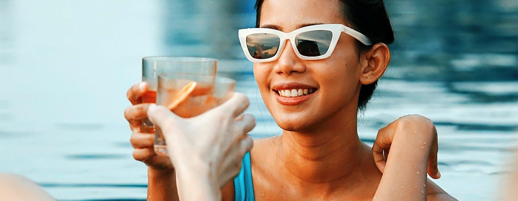 a woman in a pool holding a drink and a glass